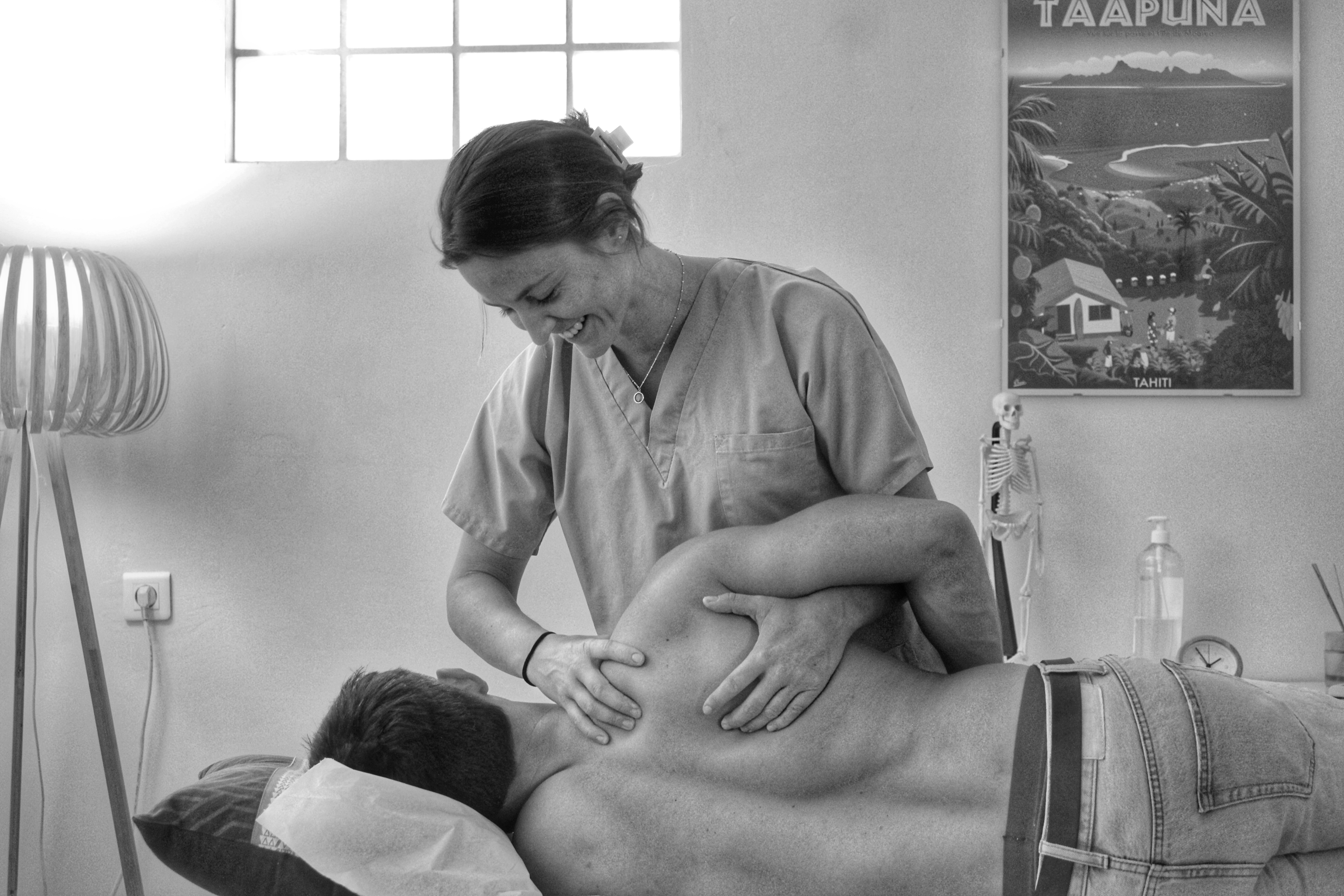 Séance d’ostéopathie : une praticienne souriante effectue une manipulation douce sur l’épaule d’un patient allongé dans un cabinet chaleureux.